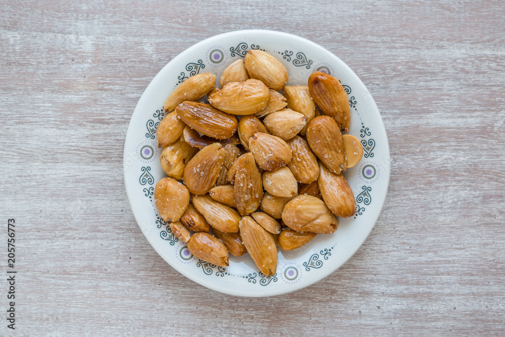 Fried almonds, typical Spanish appetizer, on a round plate on a gray wooden table. Fried almonds, typical Spanish appetizer, on a round plate on a gray wooden table.