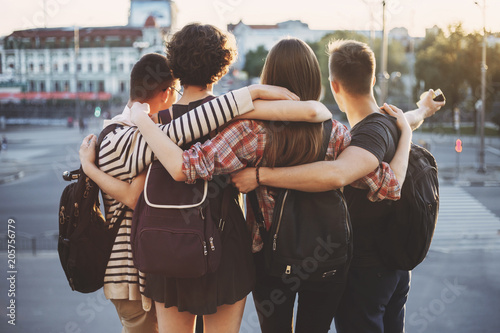 Youth, friendship, togetherness, happiness, adventure, freedom. Group of friends standing together hugging at city background