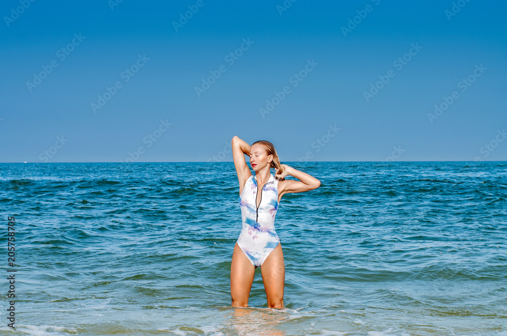 Fototapeta premium Summer. Beautiful tanned woman in swimsuit is coming out of the ocean