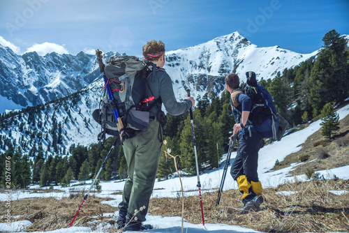 Hikers with trekking poles stand in the snowy mountains at the foot of the peak. Concept of travel and achieve the goal