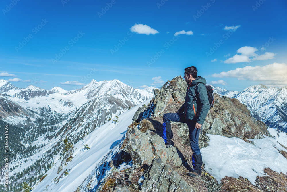 Hiker stands on top and looks up at the sky and snowy mountains around. Concept of travel and achieve the goal