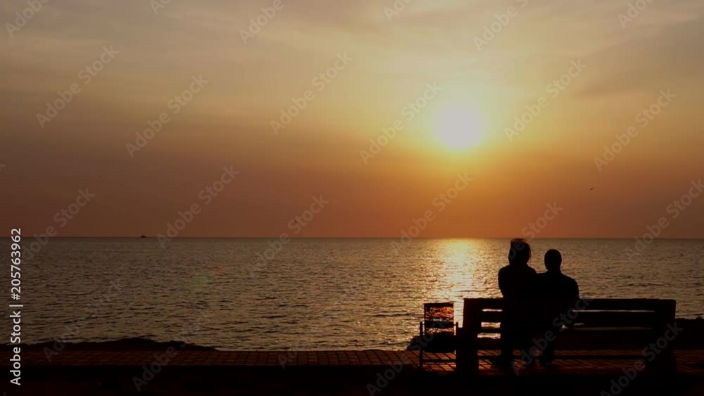 man and woman sitting on the bench watching the sunset on the sea