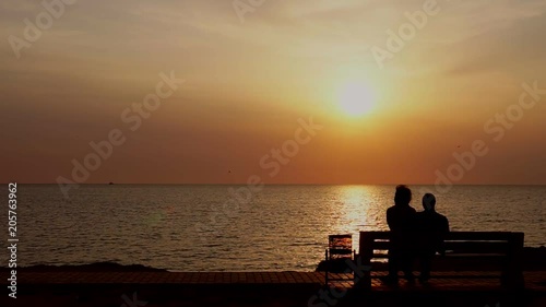 man and woman sitting on the bench watching the sunset on the sea