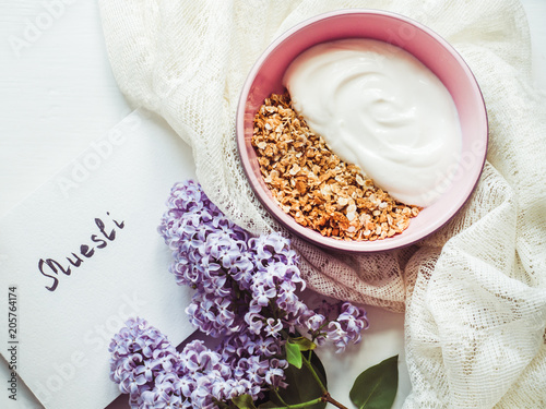 Smoothies  muesli with nuts in a beautiful plate  napkin  bouquet of blooming lilacs and notebook with an inscription on a white table. Top view  close-up.   oncept of healthy nutrition and longevity