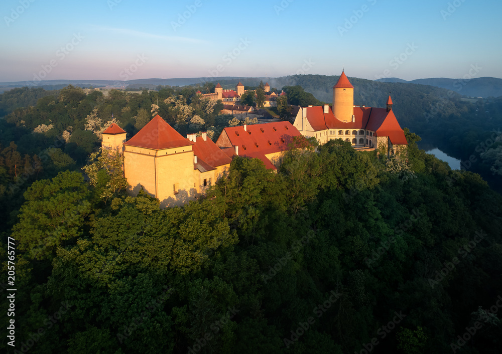 Aerial view of beautiful, Moravian royal castle Veveri or Burg Eichhorn, standing on a rock above water dam on river Svratka. Large castle above misty trees in early morning light. Aerial photography.