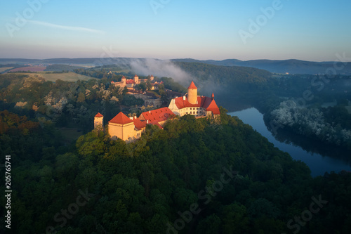 Aerial view of beautiful, Moravian royal castle Veveri or Burg Eichhorn, standing on a rock above water dam on river Svratka. Large castle above misty trees in early morning light. Aerial photography.