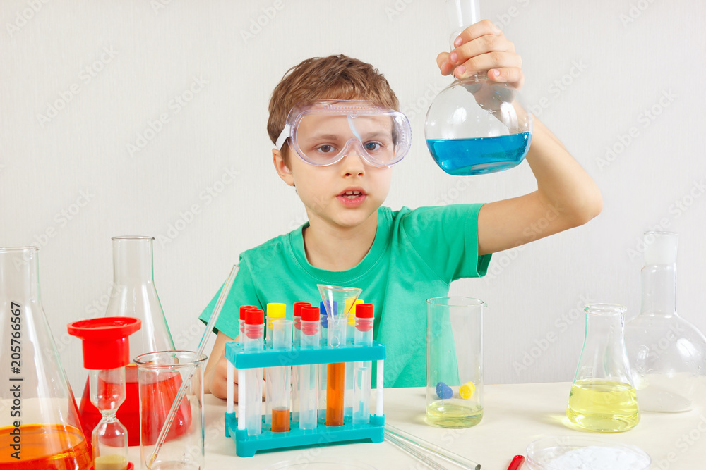 Young serious boy in safety goggles doing chemical experiments in the laboratory Young serious boy in safety goggles doing chemical experiments in the laboratory