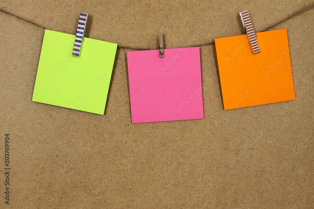  Hojas de papel de color verde, naranja y rosa (posit), sujeto con unas pequeñas pinzas de colores y dibujos, en una cuerda a pared de corcho. foto de Stock