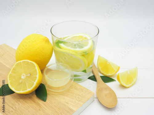 Fresh lemon in water, lemonade and lemon slice on white wood background