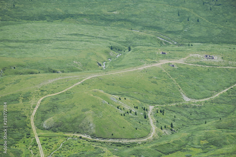 A top down view of green hills with some creeks, dirt roads and remains of buildings