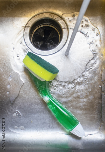 Water from tap running into stainless steel sink with pot scrubber lying in it. photo