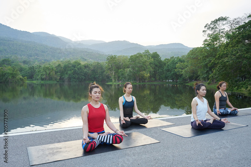 Group of women meditate near to the river and mountain background, Yoga practicing outdoors.