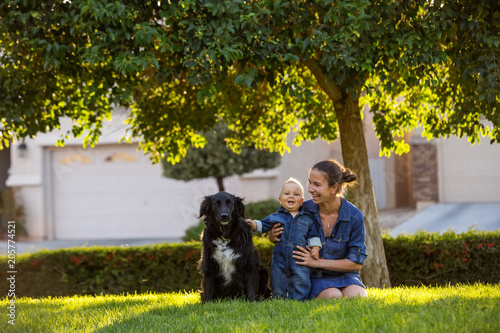 A mother with baby son and black dog in green neighborhood