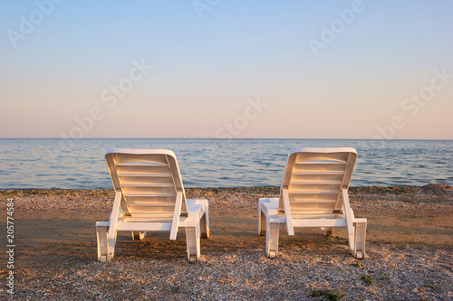 Backside view two beach chairs in the evening. Beach chaise longues beside tranquil sea on the morning. Clear sky.