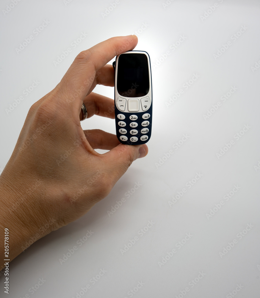 Woman hand holding the world smallest mobile phone with OLED screen in blue plastic body isolated on white Woman hand holding the world smallest mobile phone with OLED screen in blue plastic body isolated on white