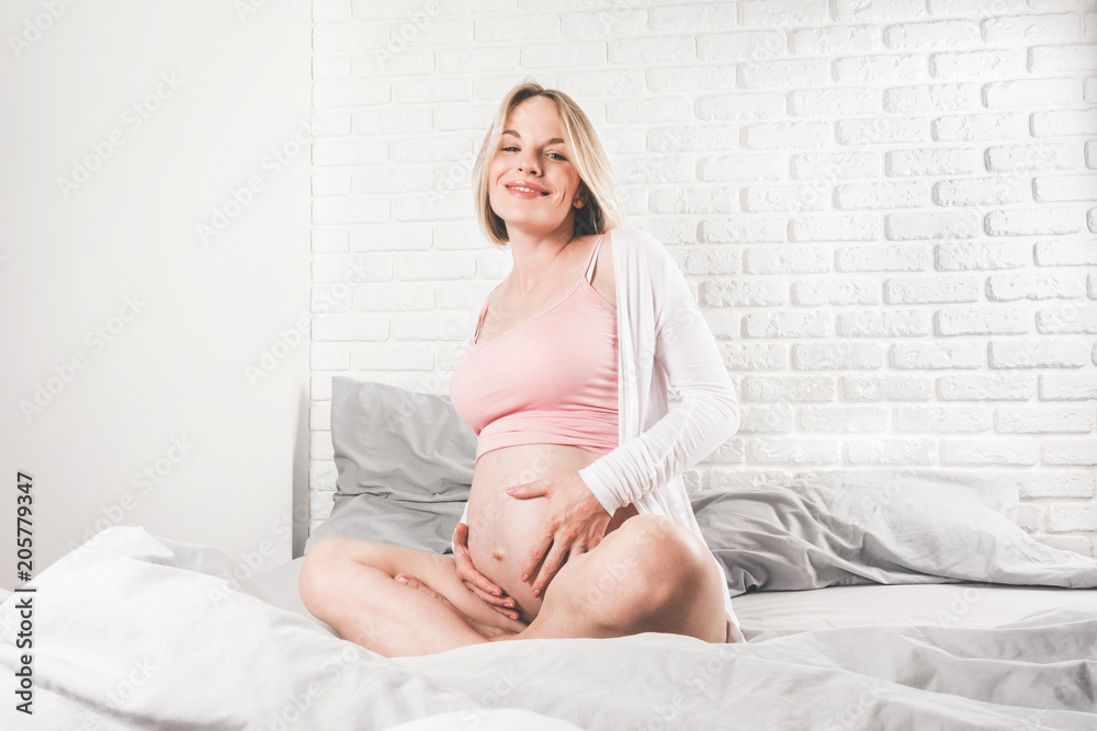 A happy young pregnant woman lies in bed in the morning and enjoys the sight of her belly and communicates with an unborn baby in her belly. Happy motherhood A happy young pregnant woman lies in bed in the morning and enjoys the sight of her belly and communicates with an unborn baby in her belly. Happy motherhood