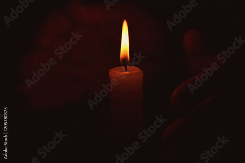 The flame of a candle warms the hands in the dark.