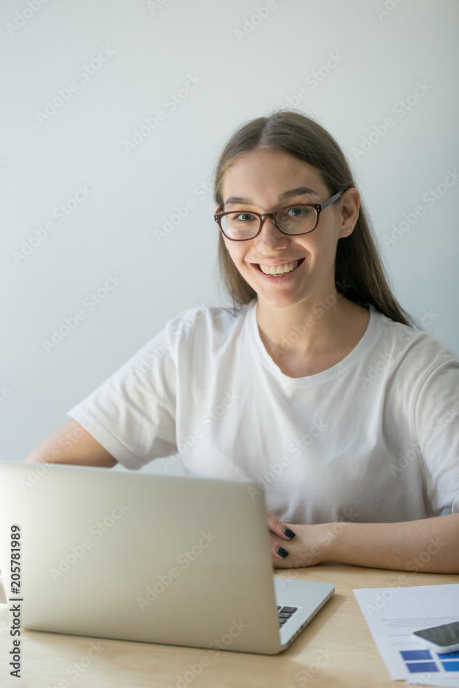Happy female professional worker posing near laptop at office desk being confident and satisfied with performed work, smiling to camera, shooting for business catalogue. Happy female professional worker posing near laptop at office desk being confident and satisfied with performed work, smiling to camera, shooting for business catalogue.
