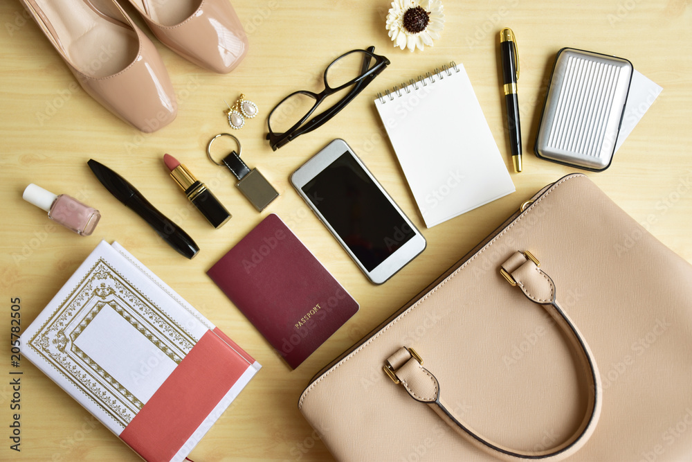 Business woman's everyday-life travel accessories flat lay on light wooden  background with formal beige handbag, shoes, a book, cellphone, blank  notepad, luxury pen, business card, glasses, cosmetics Stock Photo