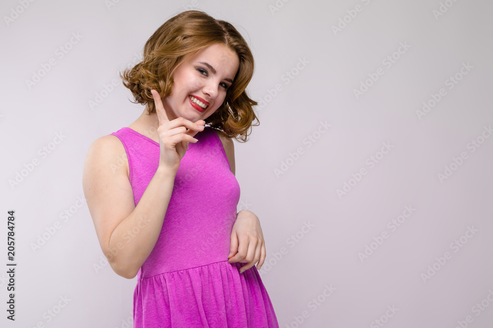 Charming young girl in pink dress on gray background. Young girl showing index finger