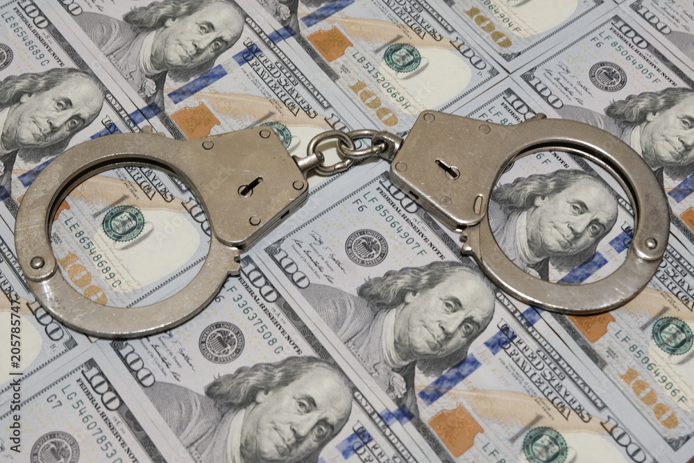Police handcuffs against a hundred dollar bills USA. Concept violation of the law, corruption, financial fraud. Police handcuffs against a hundred dollar bills USA. Concept violation of the law, corruption, financial fraud.