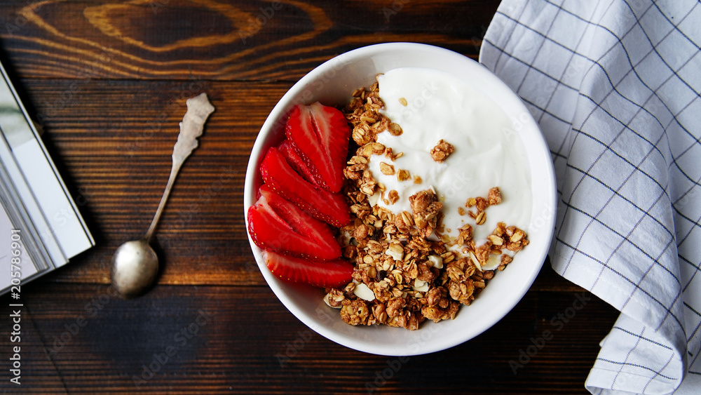 Fototapeta premium Perfect breakfast: crunchy granola with yoghurt and strawberries with a cup of black coffee on wooden table. Close up top view.