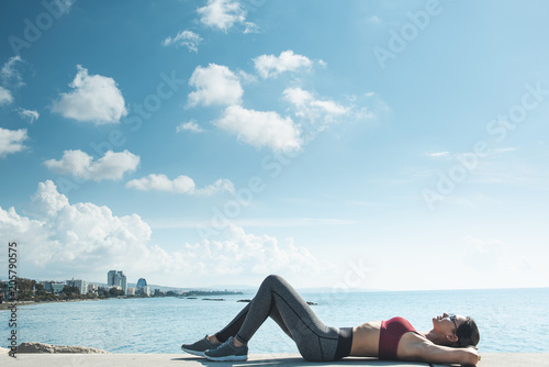 Full length side view outgoing woman lying on beach near blue sea after gymnastic exercises. Rest in open air concept © Yakobchuk Olena