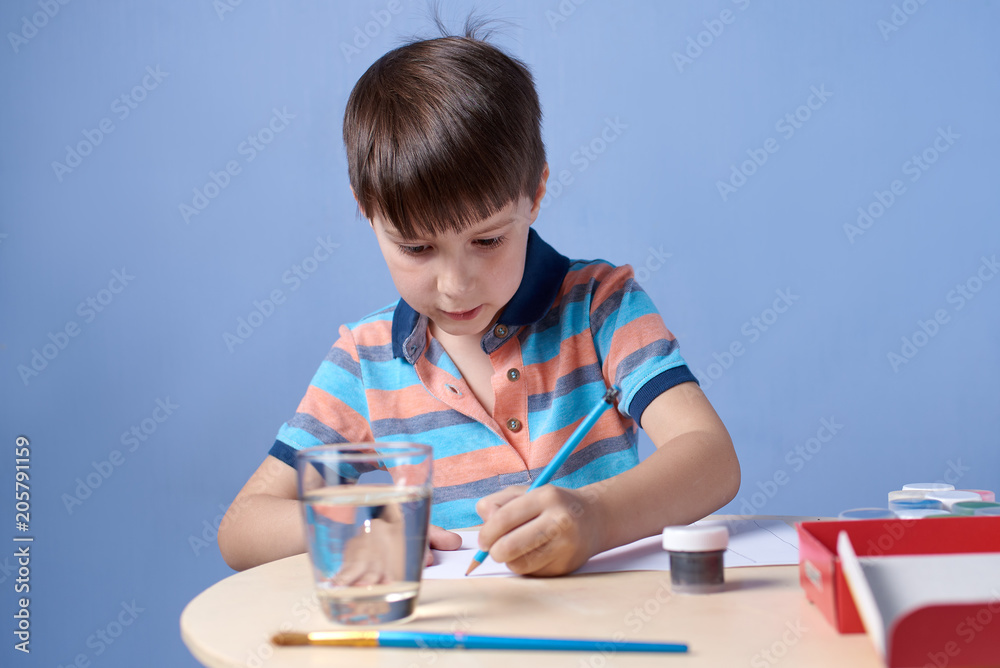 European boy carefully doing a sketch with pencil before painting with watercolors. European boy carefully doing a sketch with pencil before painting with watercolors.