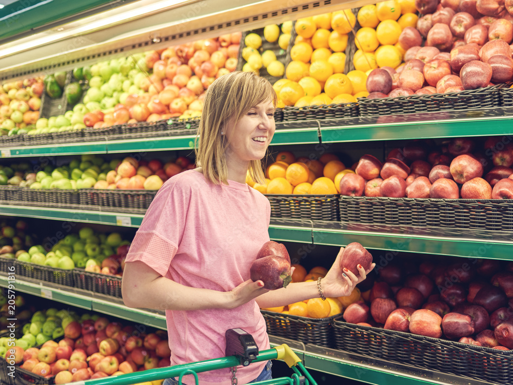 Young Caucasian woman choosing fruits during shopping at supermarket. She is smiling.