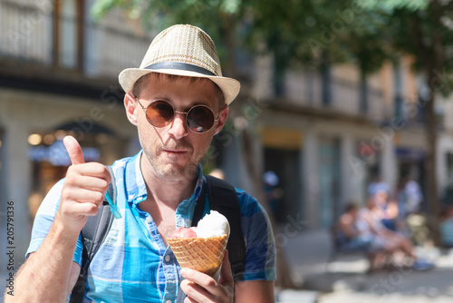 Short bearded man eating ice cream cone in a town street.