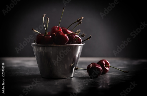 Sweet juicy cherries in metal pail on a table in front of dark background.