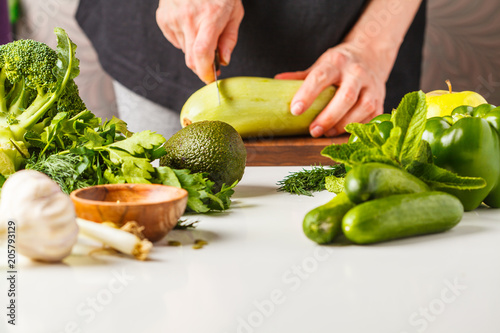 Preparation of green salad. Ingredients for salad on white table. A woman is cooking vegan food.