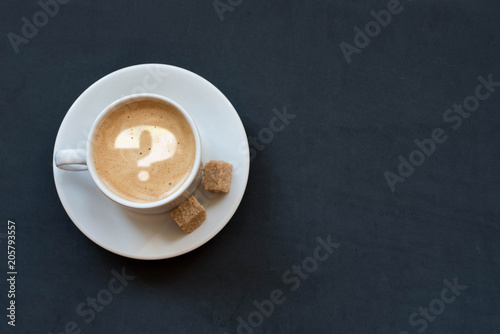 Cup of coffee with milk, cane sugar and question mark on dark background. Top view. Copy space