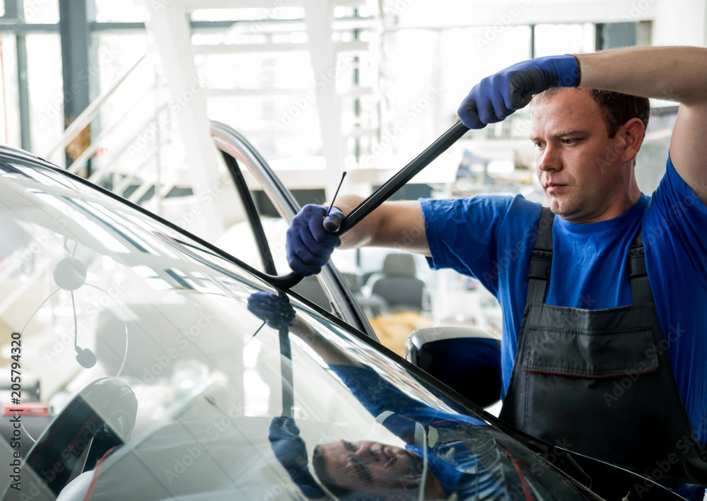 Automobile special workers remove old windscreen or windshield of a car in auto service station garage. Automobile special workers remove old windscreen or windshield of a car in auto service station garage.