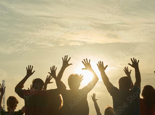 People with his hands up on the dawn. Family silhouette over sunset background.