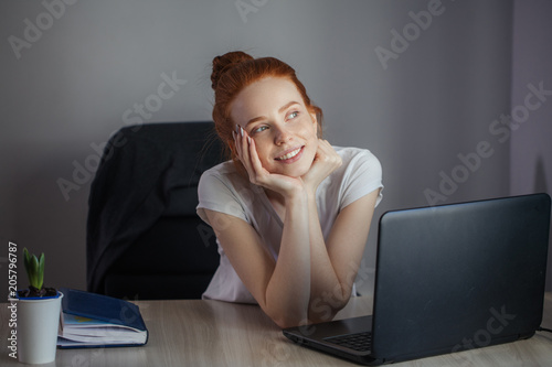 Portrait of readhaired beautiful young woman being lost in her sweet dreams sitting at the table with digital tablet photo