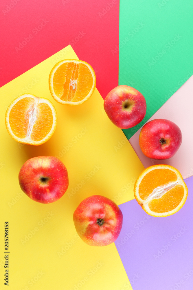Fruits of oranges and red apples on a multicolored background, halves of oranges and apples on colored paper. Copy space. Citrus in the style of pop art Fruits of oranges and red apples on a multicolored background, halves of oranges and apples on colored paper. Copy space. Citrus in the style of pop art