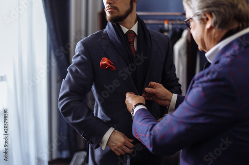 Young, handsome and successful businessman trying on a custom made stylish suit at tailors shop. Dressmaking and Tailoring establishment concept photo
