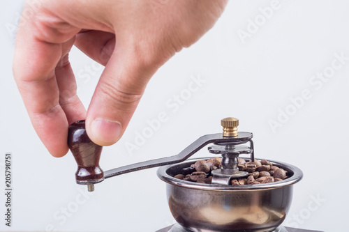 Male hand grinding coffee beans in old retro coffee mill isolated on white background. Close up, selective focus