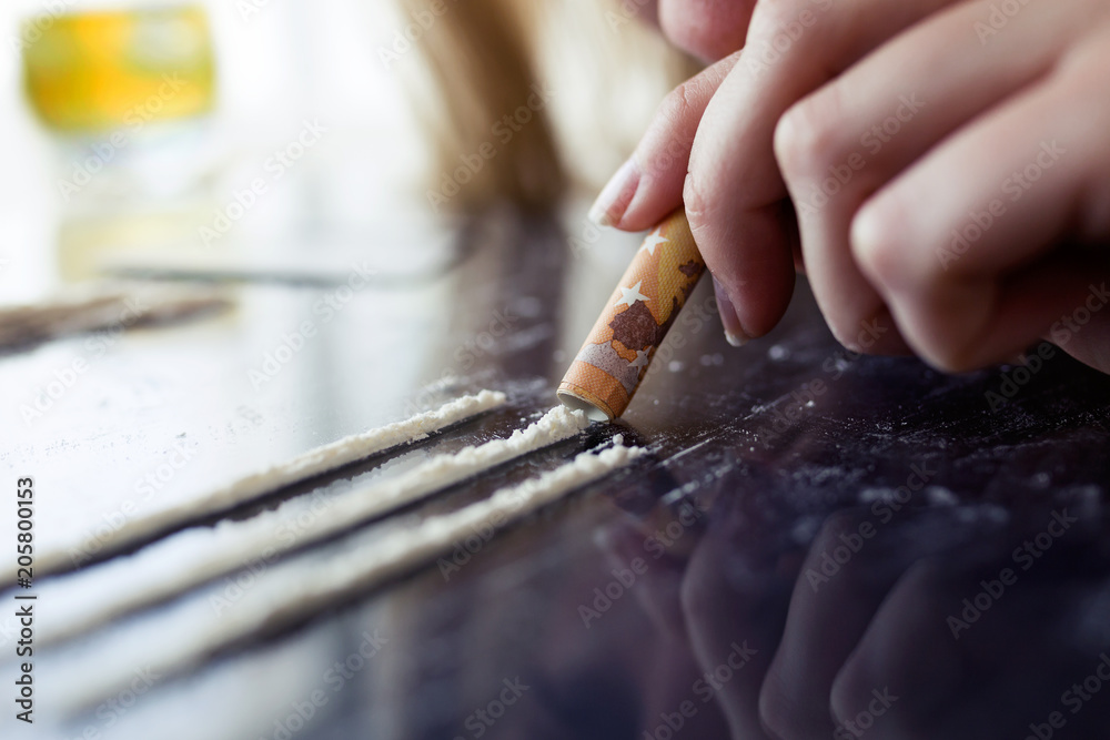 Obraz premium Young woman snorting cocaine through her nose with a rolled ticket.
