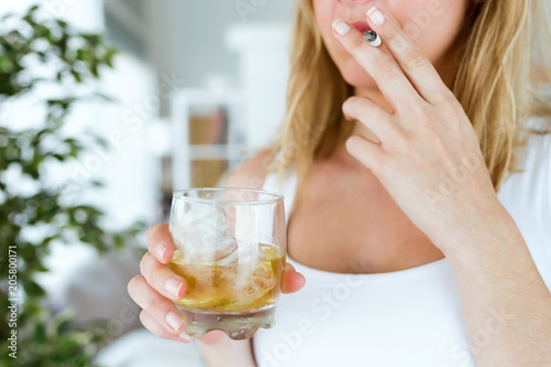 Canvastavla Young woman drinking glass of whiskey and smoking at home.