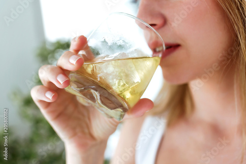 Beautiful young woman drinking glass of whiskey at home.