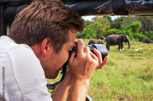 Photography Caucasian man in white shirt making photos of elephant herd during safari in nat