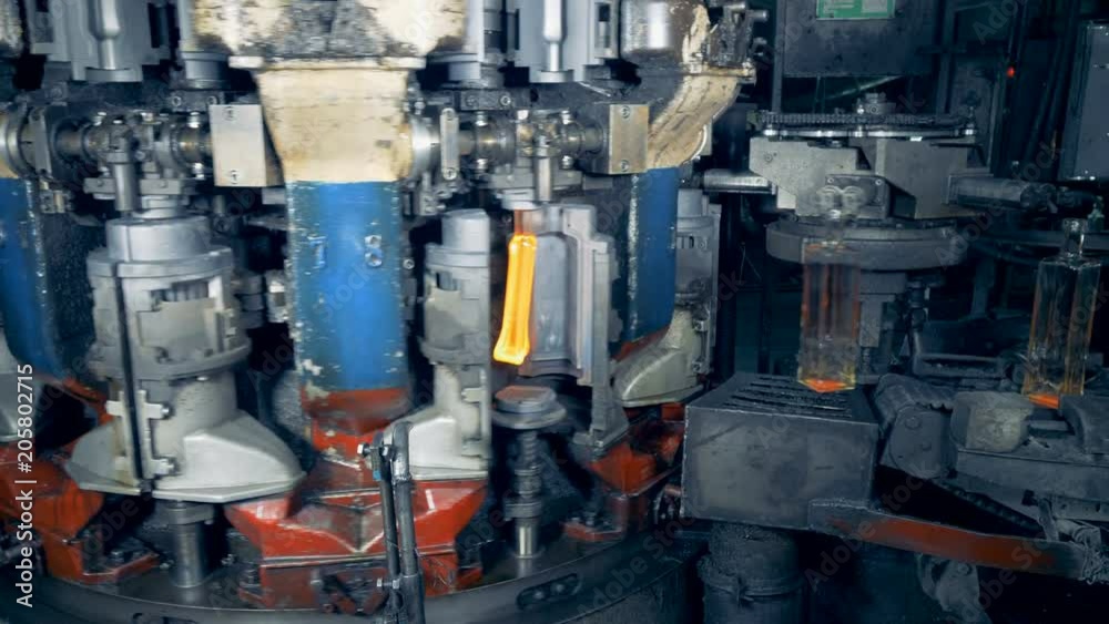 Overheated glass is being shaped into bottles which are released onto the conveyor belt Overheated glass is being shaped into bottles which are released onto the conveyor belt