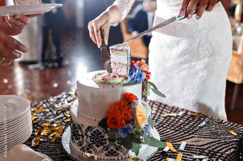 Wedding cake with flowers on table. Bride and groom cut sweet cake on banquet in restaurant.