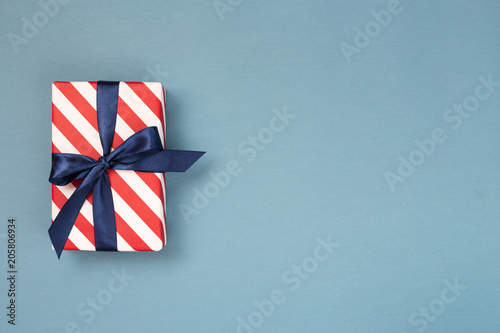 One gift box wrapped in red striped paper and tied with blue bow on blue-gray...