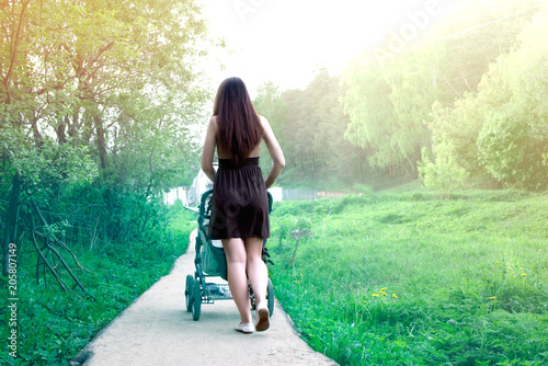 Girl walking with a baby stroller. Back view.