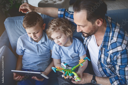 Photos Top view concentrated kids and focused adult looking at digital device in room