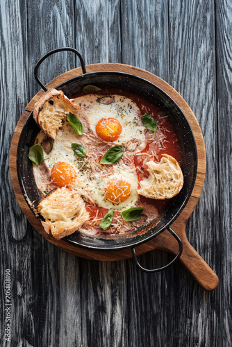 top view of delicious fried eggs with cheese, bread and sauce in pan on wooden cutting board