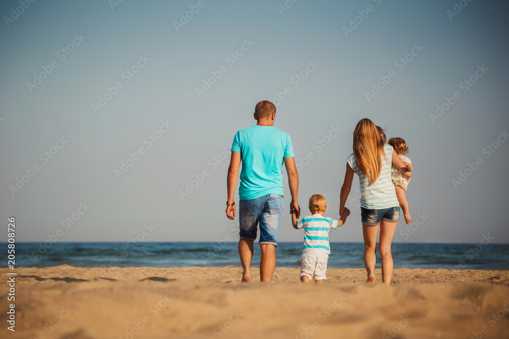 Young happy loving family with small kids walking at beach together near the ocean, happy lifestyle family concept. Back view